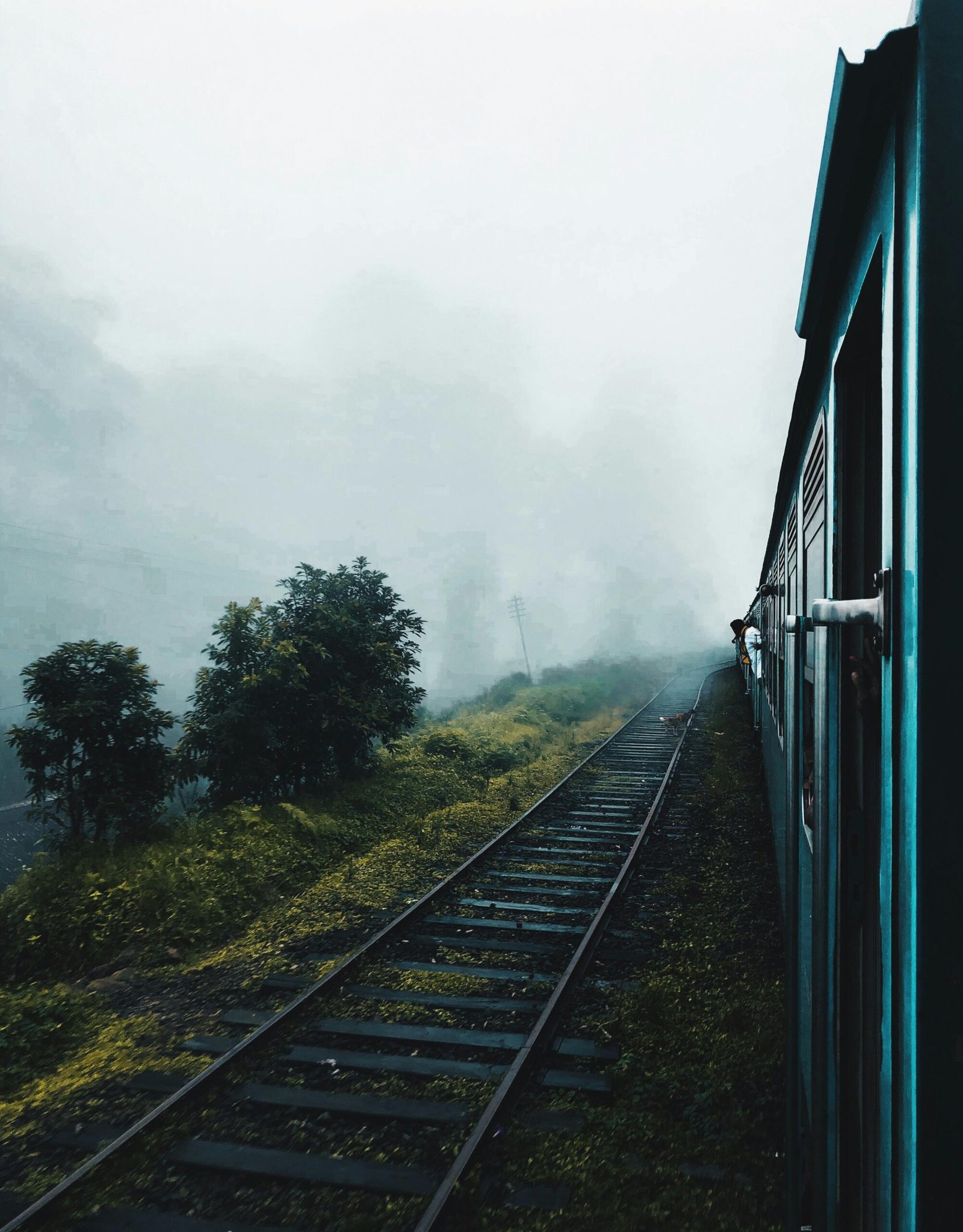 A train travels through a foggy countryside with railway tracks disappearing into the mist.