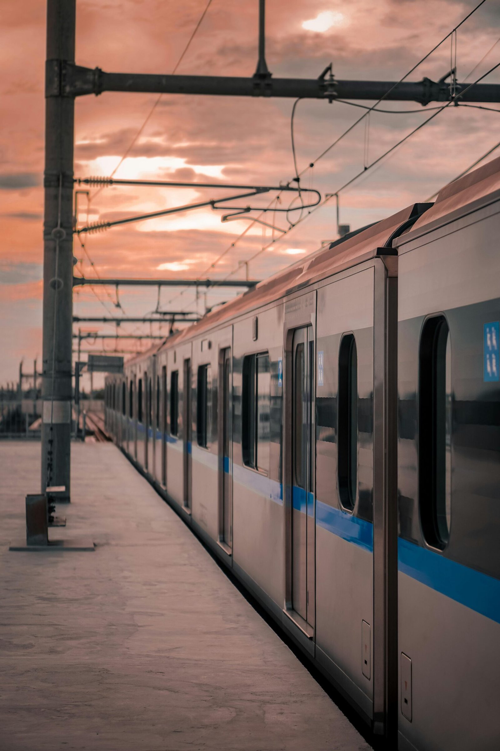 A sleek modern train waits at a railway platform during a vibrant sunset, showcasing public transportation.